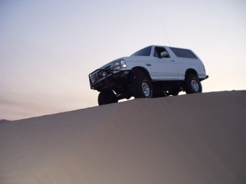 1993 Ford Bronco - A 1993 Ford Bronco navigates a sandy incline under a clear sky.