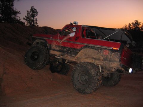 1979 Ford Bronco - A red 1979 Ford Bronco is shown navigating a steep, muddy incline as the sun sets.