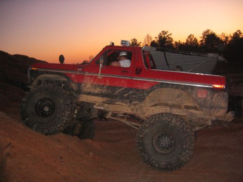 1979 Ford Bronco - A red SUV with off-road modifications navigates a dirt incline during twilight.