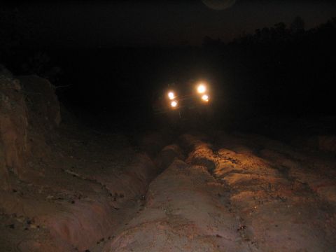 1979 Ford Bronco - Headlights cut through the darkness as a vehicle navigates a challenging, uneven dirt path.
