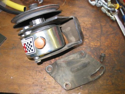 1981 Ford Bronco - A chrome power steering pump with a checkered sticker and its associated mounting bracket are shown on a wooden surface.