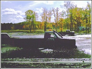 1976 Chevrolet Silverado 2500 - Two trucks are stuck in a muddy field with trees in the background.