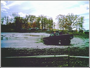 1976 Chevrolet Silverado 2500 - A dark pickup truck is stuck in a muddy area, with the SuperMotors logo in the foreground.
