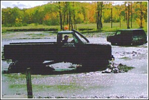 1976 Chevrolet Silverado 2500 - A pickup truck navigates a muddy terrain with another vehicle visible in the distance.