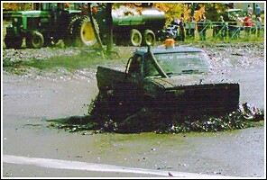 1976 Chevrolet Silverado 2500 - A truck is stuck in a muddy area, with a tractor and trailer visible behind it.