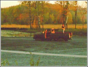 1976 Chevrolet Silverado 2500 - A pickup truck is seen driving through a field with a person standing in the bed.