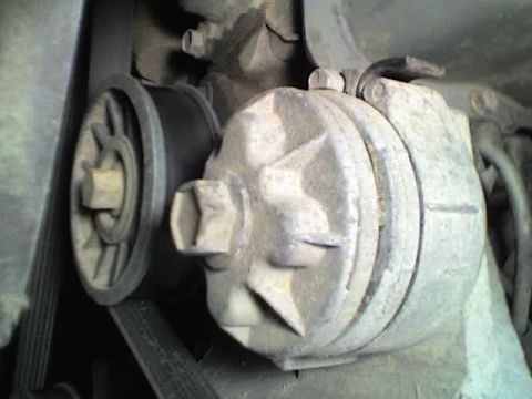 1989 Ford Bronco - Close-up of a grimy cast-aluminum air conditioning compressor mounted in an engine bay, with its clutch pulley driven by a black multi-rib…