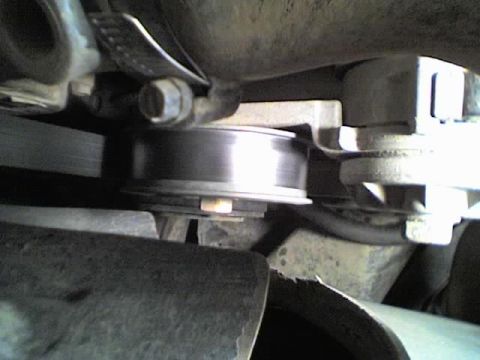 1989 Ford Bronco - Tight close-up under the hood of a smooth steel serpentine-belt idler pulley and its mounting bolt, with the ribbed accessory belt running…
