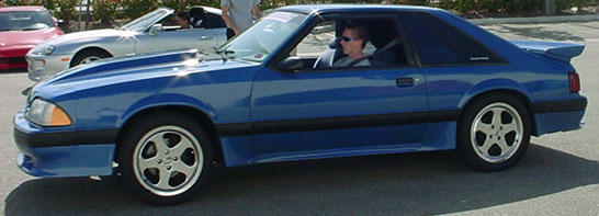 Blue coupe with a spoiler, side view. Appears to be from the late 1980s