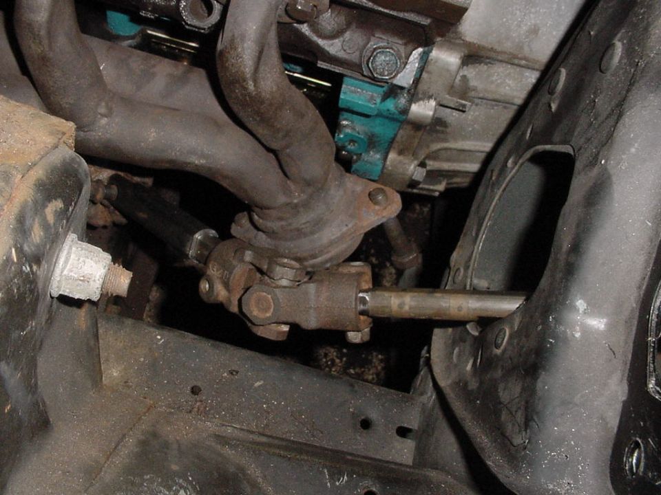 Steering shaft U-joint and rusty exhaust manifold near teal engine block, viewed from under the hood