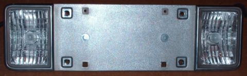 2000 Jeep Cherokee - A license plate bracket with integrated headlights is shown against a wooden background.