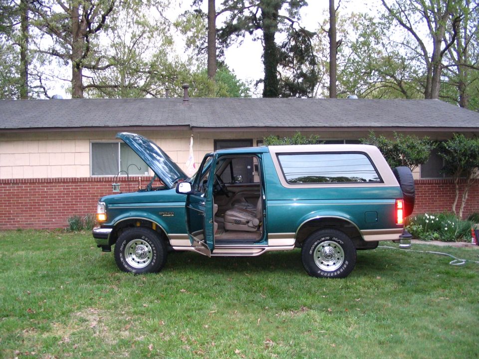 Teal and tan Ford Bronco SUV side view on grass with hood up and driver door open