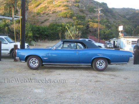 1968 Ford Mustang - A blue convertible with a black top is parked on a dirt lot next to a white SUV.
