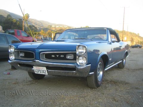 1968 Ford Mustang - A blue 1967 Pontiac GTO convertible is parked on a dirt lot with a hillside in the background.