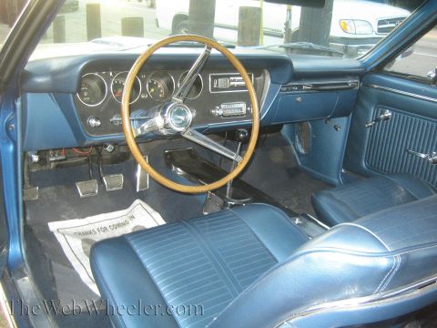 1968 Ford Mustang - The interior of a blue 1967 Pontiac GTO, a wood-rimmed steering wheel and distinctive GTO badging on the dashboard.