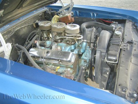 1968 Ford Mustang - Close-up view of a blue car's engine compartment, showing the carburetor setup and cooling fan.