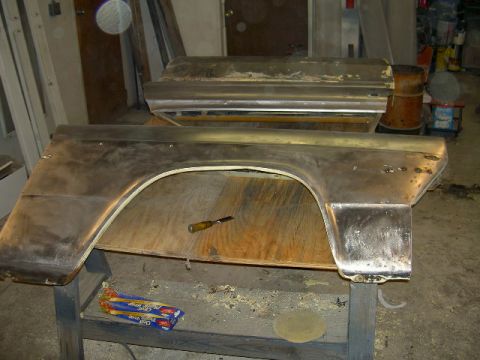 1967 Ford Ranchero - Car parts, likely a fender and door, sit on a workbench in a garage.