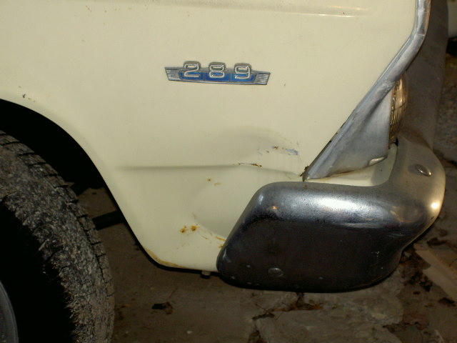 Close-up of a cream-colored car fender with a '289' badge and a chrome bumper. Some rust is visible