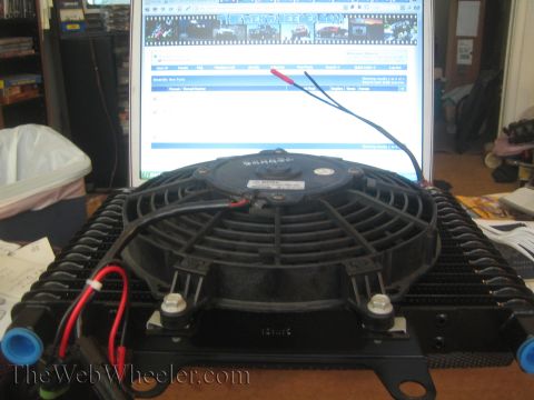 1990 Ford Bronco - black electric fan mounted on a finned oil cooler with red and black wiring, sitting in front of a computer monitor.