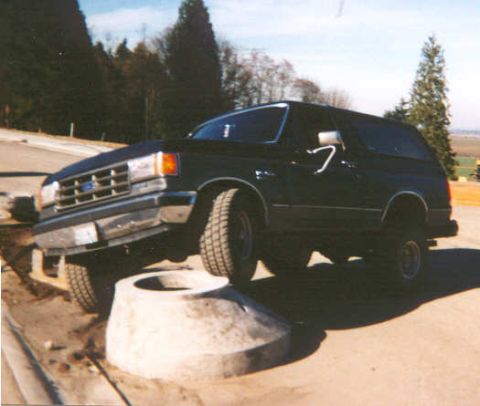 1988 Ford Bronco - Black Ford Bronco navigates an off-road obstacle with its front passenger tire elevated.
