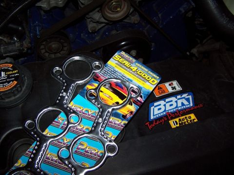 2000 Ford Crown Victoria - Exhaust gaskets and various performance part stickers are displayed on a dark engine cover.