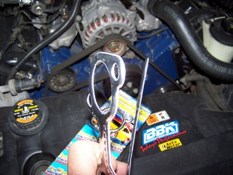 2000 Ford Crown Victoria - Exhaust gasket held up in front of a car engine bay with visible alternator and belts.
