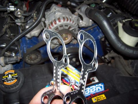 2000 Ford Crown Victoria - Close-up of exhaust gaskets held in front of a vehicle's engine compartment.