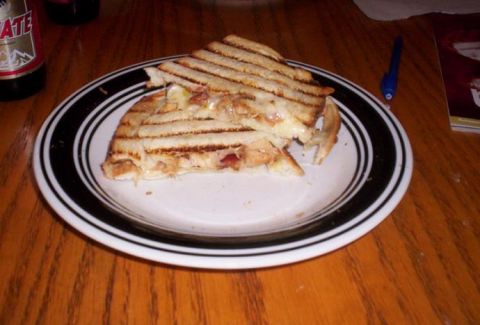 1989 Ford Bronco - A grilled sandwich sits on a plate on a wooden table, next to a bottle and a pen.