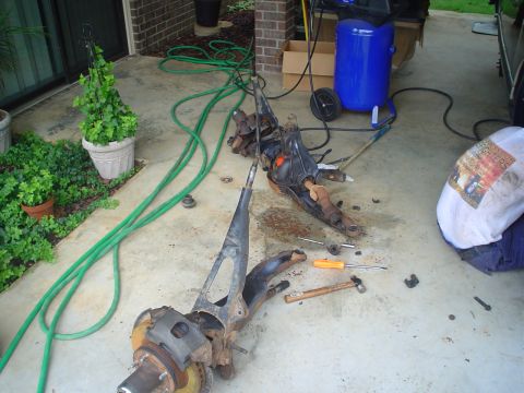 1984 Ford Bronco - Vehicle suspension parts are disassembled and laid out on the ground, with tools nearby.