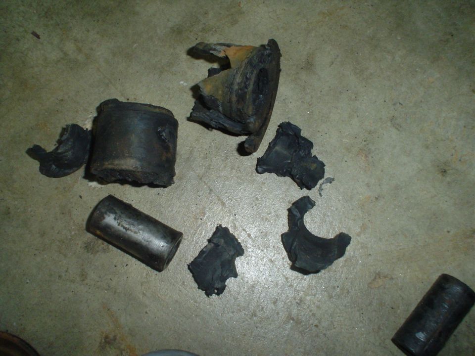 Old cracked rubber suspension bushings and steel inner sleeves removed and laid on concrete floor