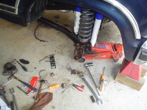 1984 Ford Bronco - Suspension work in progress on a blue vehicle, showing new shocks, springs, and various tools scattered around.