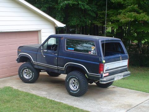 1984 Ford Bronco - This lifted 1984 Ford Bronco, seen from a 3/4 front angle, is parked in a driveway next to a garage.