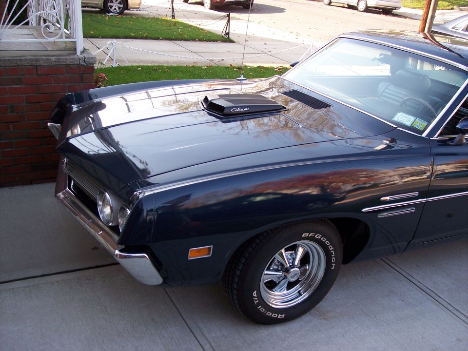 Dark blue-green classic Ford with Cobra Jet hood scoop and chrome mag wheels on driveway