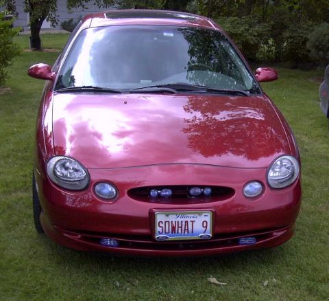 1997 Ford Taurus - A red sedan is parked on grass in front of a house, showing its front end and license plate.