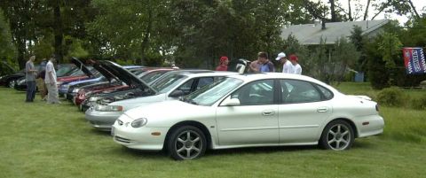 1997 Ford Taurus - A line of cars, including a white 1997 Ford Taurus, are parked on a grassy lawn.