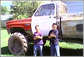 1976 Chevrolet Silverado 2500 - A modified pickup truck with oversized tires is shown with two children posing in front of it.