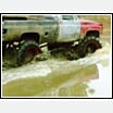 1976 Chevrolet Silverado 2500 - A truck navigates a muddy terrain, its large tires kicking up water and mud.
