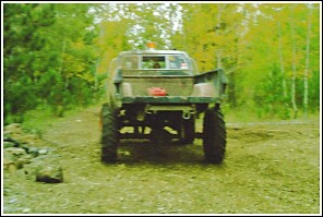 1976 Chevrolet Silverado 2500 - A heavily modified pickup truck with oversized tires is shown from behind in a rural, wooded setting.