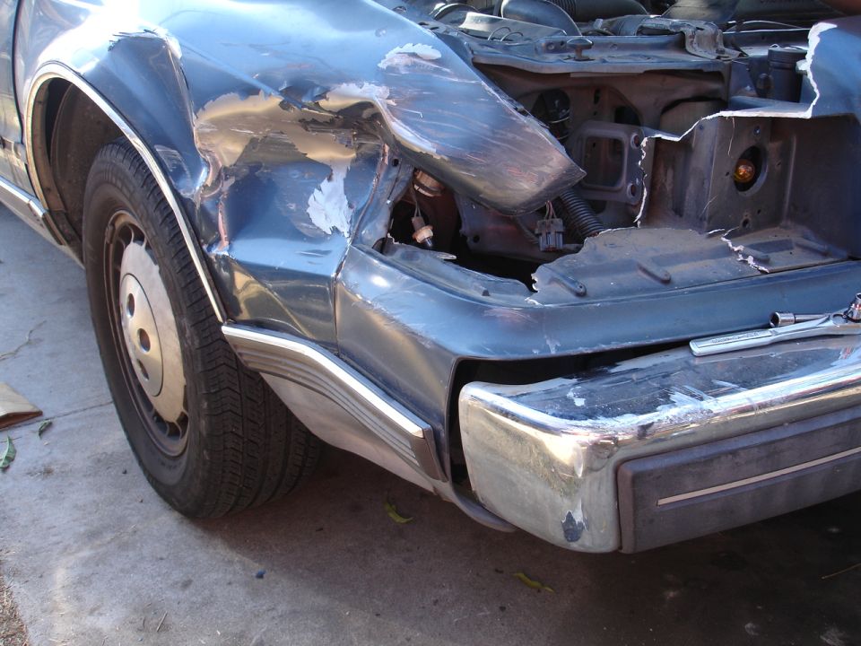 Crumpled and torn right front fender on light blue sedan, headlight missing
