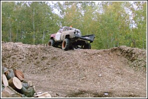 1976 Chevrolet Silverado 2500 - A heavily modified pickup truck navigates a terrain of wood chips, suggesting off-road use.
