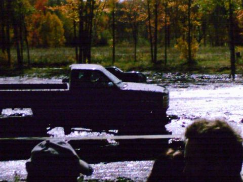 1976 Chevrolet Silverado 2500 - A dark pickup truck navigates a muddy terrain during a mud run event, with another vehicle visible in the background.
