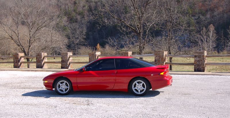 Red coupe parked on gravel with a stone and wood fence behind it