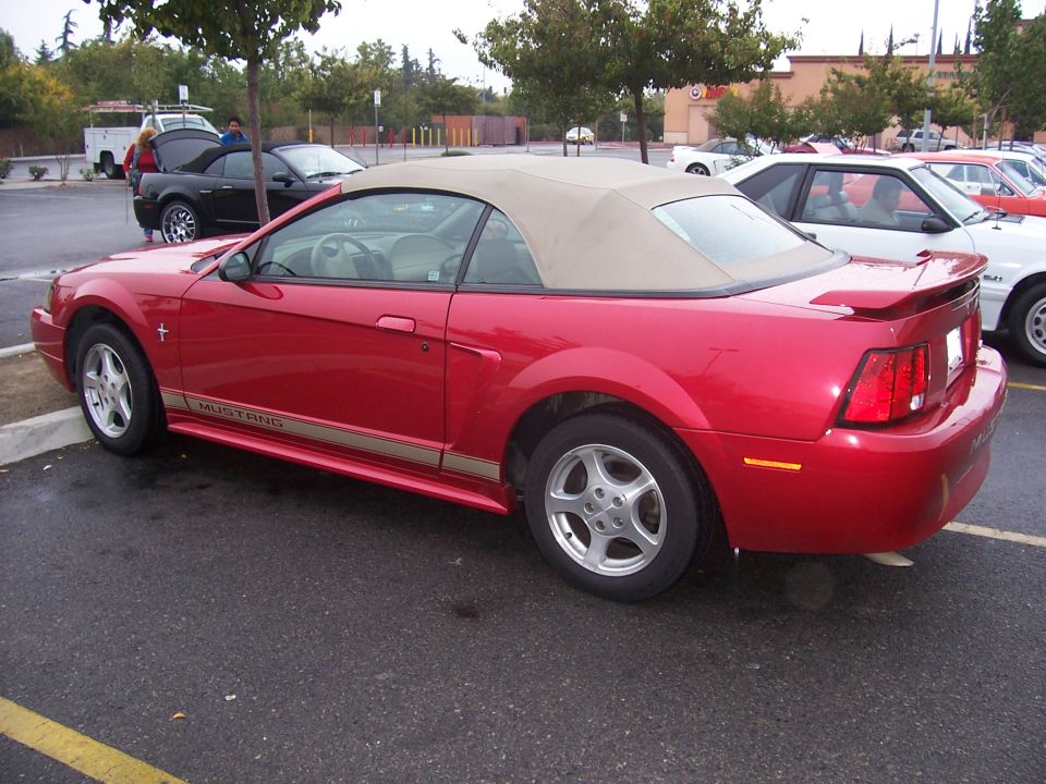 Red convertible Mustang with tan top, side view. "Mustang" text on lower body