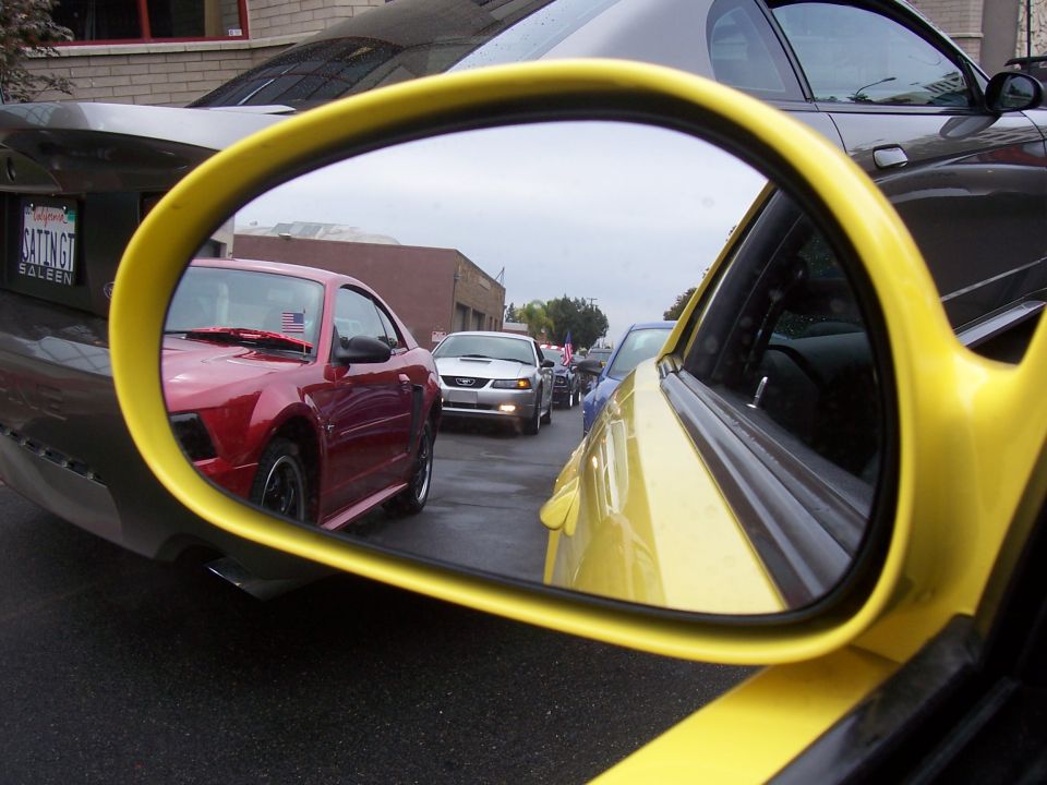 Red Mustang and silver Mustang in traffic, viewed in yellow car's side mirror