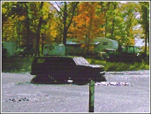 1976 Chevrolet Silverado 2500 - A dark SUV navigates through a muddy terrain, with campers and trees visible in the background.