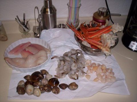 1989 Ford Bronco - Raw seafood laid out on a kitchen counter: white fish fillets in a fluted dish, clams, peeled shrimp, scallops and a steel bowl of crab leg…