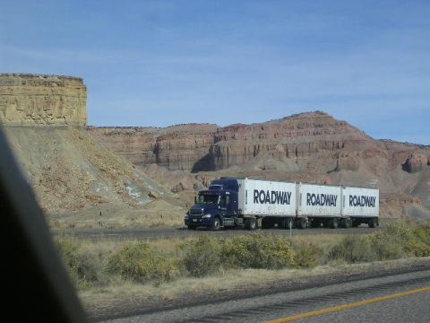 1975 Ford Ranchero - A Roadway semi-truck travels down a highway through a desert landscape with large rock formations.