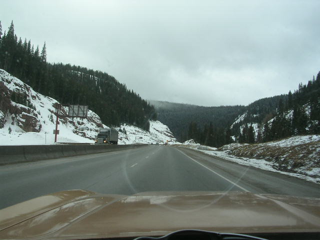Brown car dashboard and windshield view on a snowy mountain highway with a truck ahead