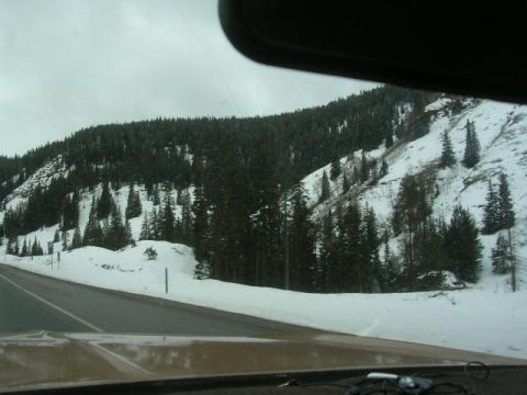 1975 Ford Ranchero - View from inside a vehicle traveling on a snowy mountain road, with evergreen trees covering the slopes.