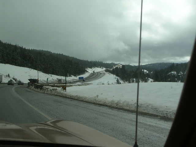 View from a car on a snowy highway with trees and other vehicles